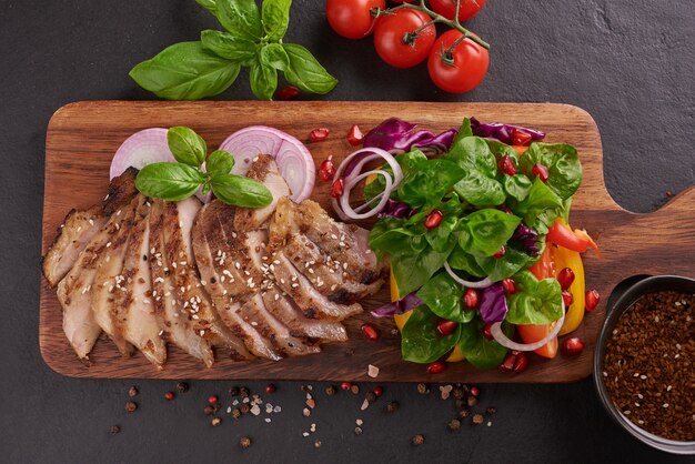 Bife grelhado com vegetais frescos, pimentão, tomate, cebola roxa, pimenta rosa e especiarias. Comida saborosa feita em casa. Conceito de refeição saborosa e saudável. Superfície de pedra preta. Bife de porco com salada