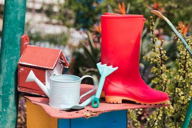 Birdhouse com botas vermelhas wellington; regador; ferramentas de jardinagem no jardim