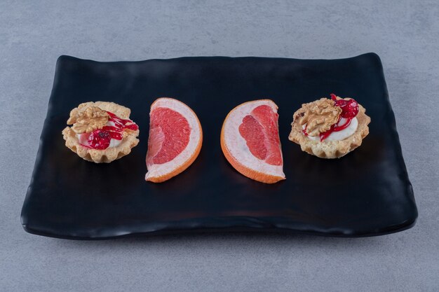 Biscoito delicioso com fatias de toranja na placa preta sobre superfície cinza