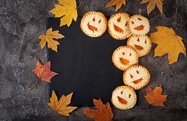 Biscoitos caseiros na forma de abóboras de jack-o-lanterna de Halloween na mesa escura. Vista do topo.