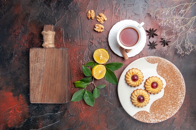 Biscoitos com uma xícara de chá em um bolo de biscoito de açúcar de mesa escura com vista de cima