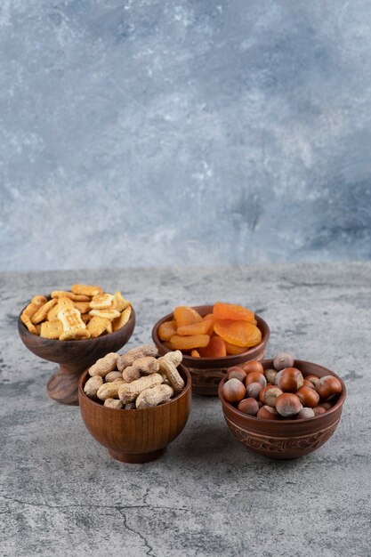 Biscoitos, damascos secos, avelãs e amendoins em tigelas de madeira.