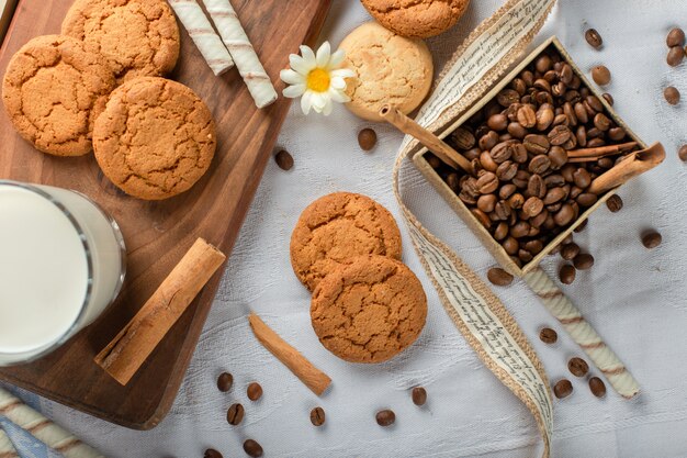 Biscoitos de aveia com um copo de leite e caixa de grãos de café.