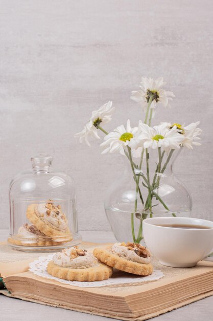 Biscoitos de aveia, uma xícara e margaridas no livro.