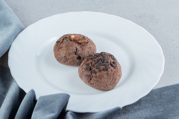 Biscoitos de chocolate em uma travessa branca ao lado da toalha de mesa no fundo de mármore.