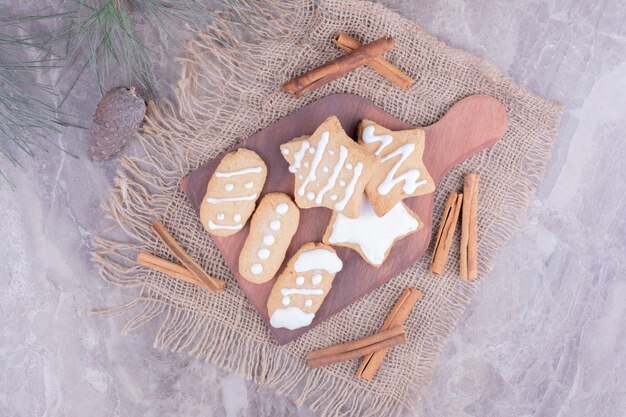 Biscoitos de gengibre em formas de estrela e oval com paus de canela na travessa de madeira.