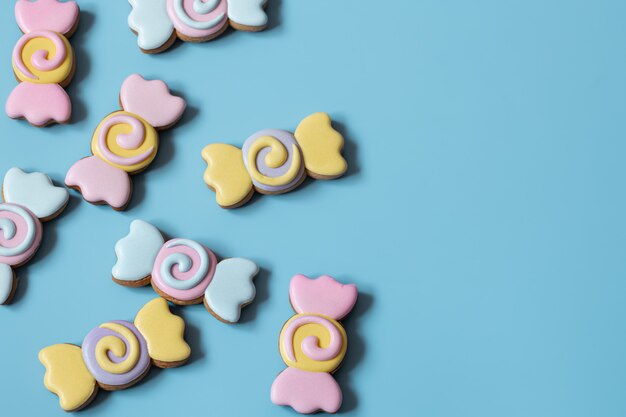 Biscoitos de gengibre festivos coloridos na forma de doces cobertos com esmalte em um espaço de cópia de fundo azul.