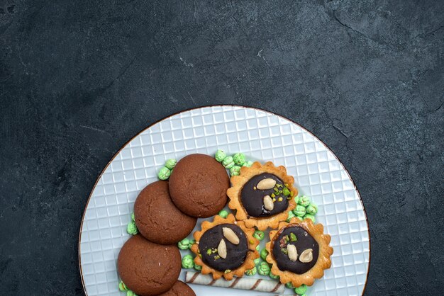 Foto grátis biscoitos deliciosos com doces em cima de biscoitos de mesa cinza-escuro bolo de confeitaria