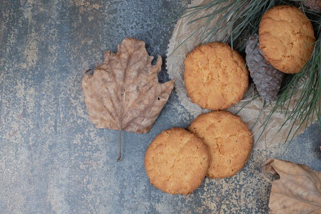 Biscoitos deliciosos com folhas e pinha na mesa de mármore.