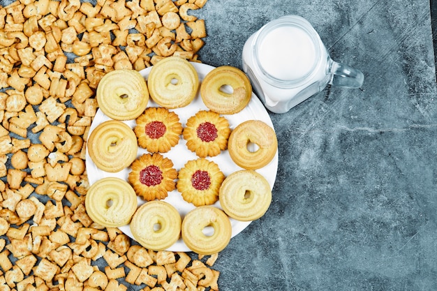 Biscoitos do alfabeto espalhados, um prato de biscoitos e um pote de leite na mesa de mármore.