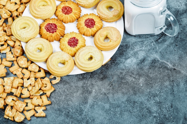 Biscoitos do alfabeto espalhados, um prato de biscoitos e um pote de leite na mesa de mármore.