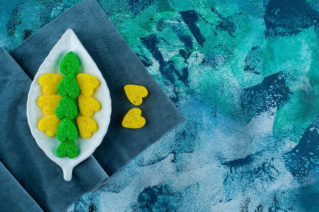 Biscoitos doces amarelos e verdes num prato sobre um pedaço de tecido, sobre o fundo azul.