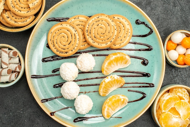 Biscoitos doces com balas de coco e frutas em cima da mesa cinza