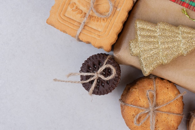 Biscoitos doces em corda com presente e brinquedo dourado de Natal na superfície branca