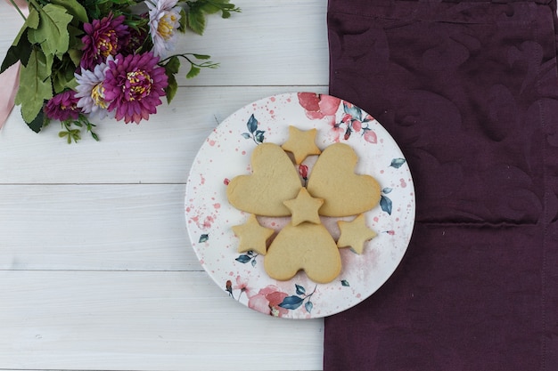 Biscoitos em um prato com flores planas sobre fundo de madeira e tecido