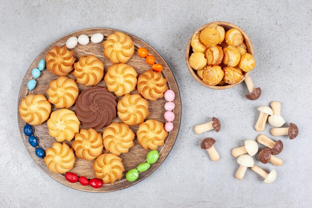 Biscoitos em uma bandeja de madeira rodeada de doces e em uma tigela com molho de cogumelos de chocolate espalhados no fundo de mármore. Foto de alta qualidade