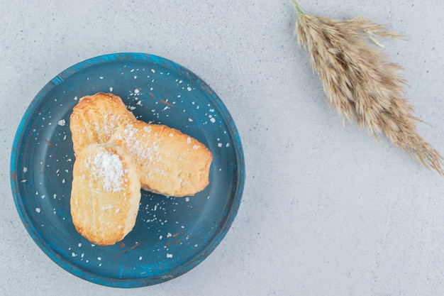 Biscoitos escamosos em uma bandeja azul ao lado de um talo de grama no fundo de mármore.