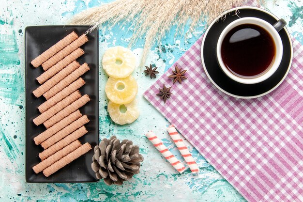 Biscoitos longos doces com uma xícara de chá e anéis de abacaxi secos no fundo azul.