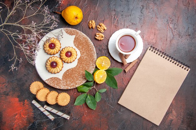 Biscoitos pequenos com uma xícara de chá na mesa escura, bolo de açúcar, biscoito doce