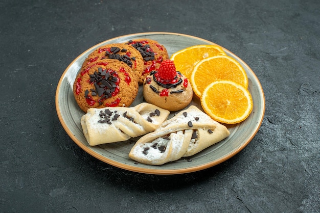 Biscoitos saborosos de frente com pastéis de frutas e fatias de laranja na superfície escura frutas bolo doce torta chá açúcar