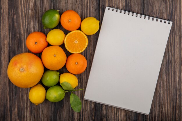 Bloco de notas de cópia de vista de cima com limão, laranja, limão e lima em fundo de madeira