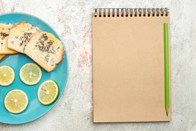 Foto grátis bloco de notas de pão com creme de limão e lápis verde fatiado com frutas cítricas e pão branco no prato