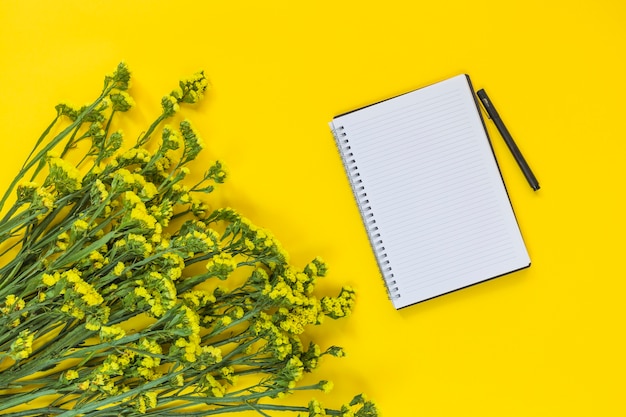 Foto grátis bloco de notas em espiral e caneta perto do monte de flores frescas em fundo amarelo