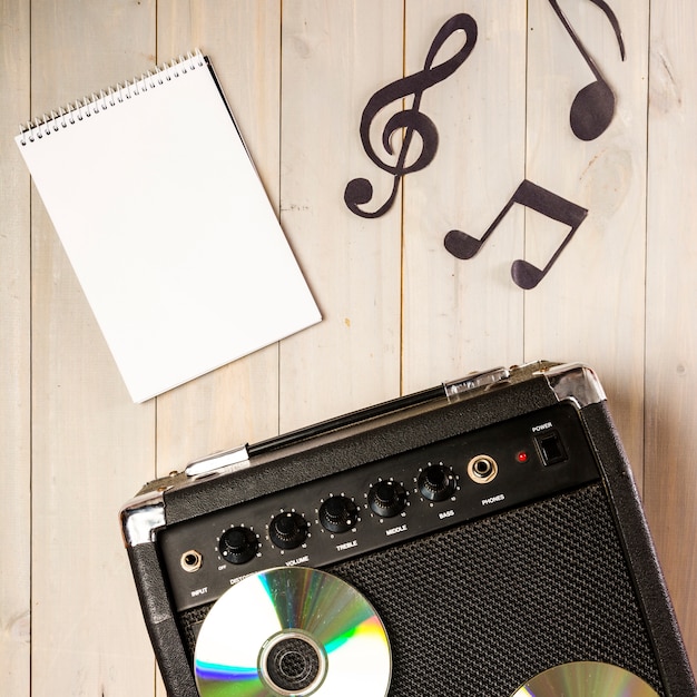 Foto grátis bloco de notas em espiral; nota musical e amplificador com disco compacto na mesa de madeira