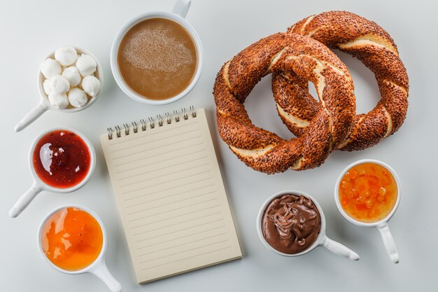 Bloco de notas plana leiga e uma xícara de café com geléias, framboesa, açúcar, chocolate em xícaras, pão turco na superfície branca