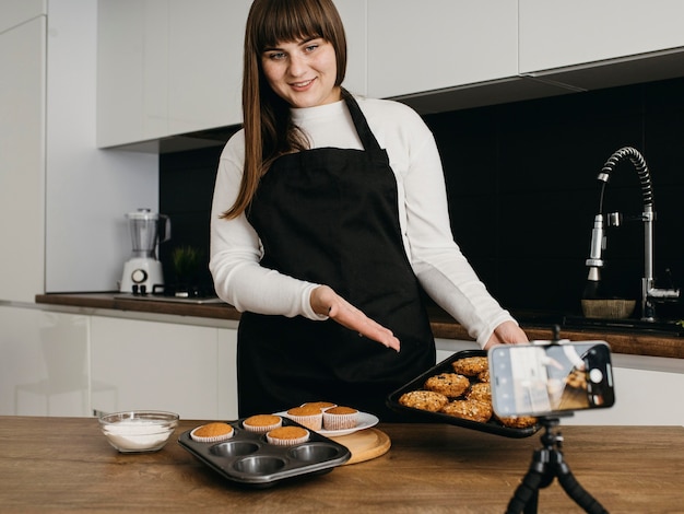 Blogueira sorridente gravando a si mesma enquanto prepara muffins