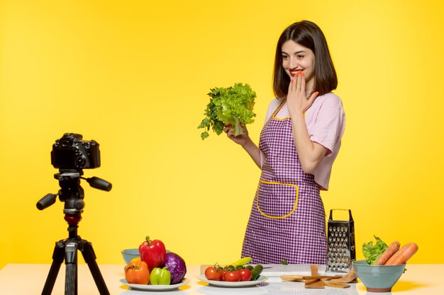 Blogueiro de comida fofo e adorável chef em avental rosa gravando vídeo para mídias sociais cobrindo a boca feliz