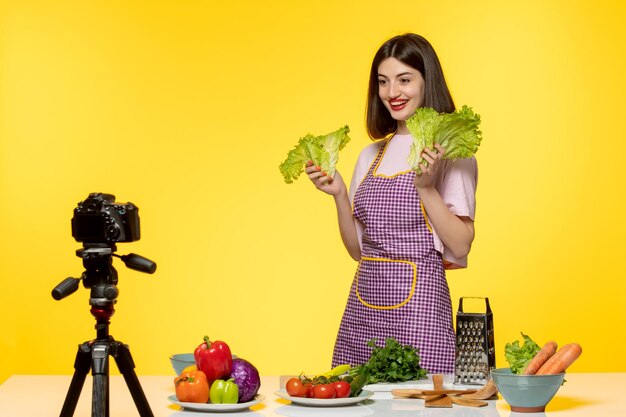 Blogueiro de comida linda garota adorável em avental rosa gravando vídeo para mídias sociais segurando verdes