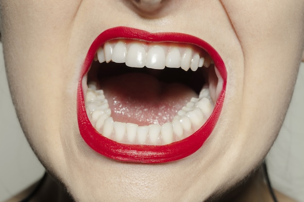Boca feminina de close-up com maquiagem de lábios de brilho vermelho brilhante.