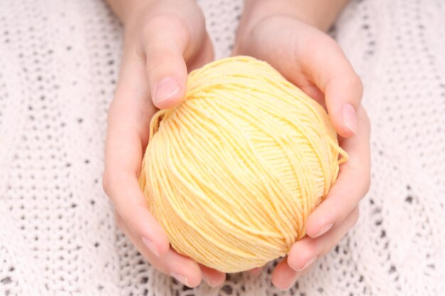 Bola amarela de lã nas mãos no contexto de uma toalha de mesa de malha branca. foto de alta qualidade