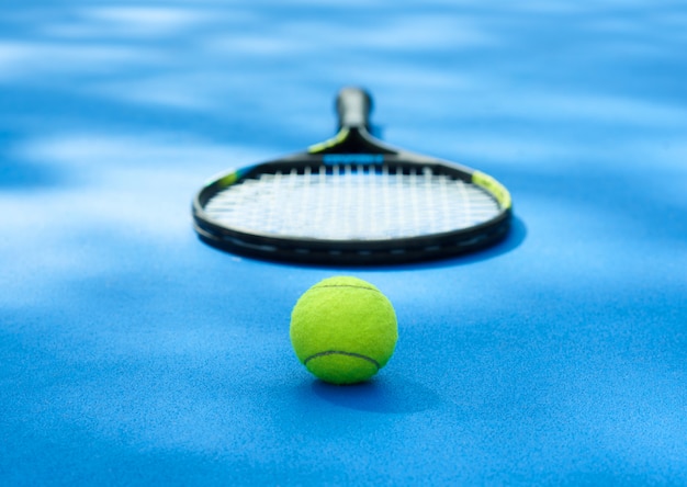 Bola amarela está deitada no tapete de quadra de tênis azul com raquete profissional.