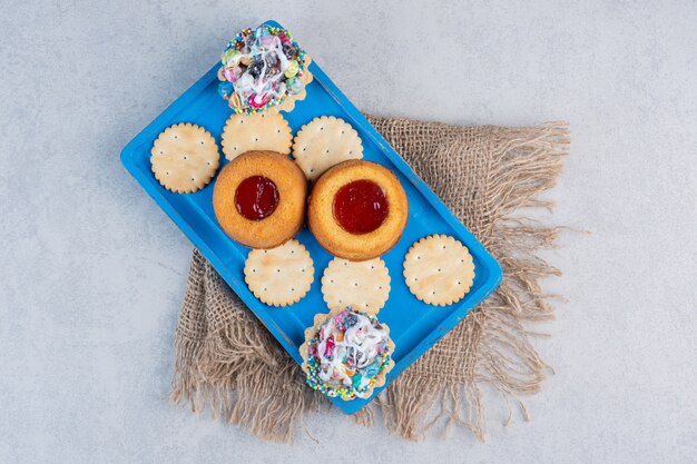 Bolachas, cupcakes e bolos recheados de geleia em uma travessa azul na mesa de mármore.