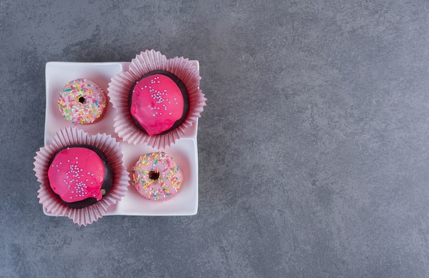 Bolas de chocolate com esmalte rosa e donuts na chapa branca.