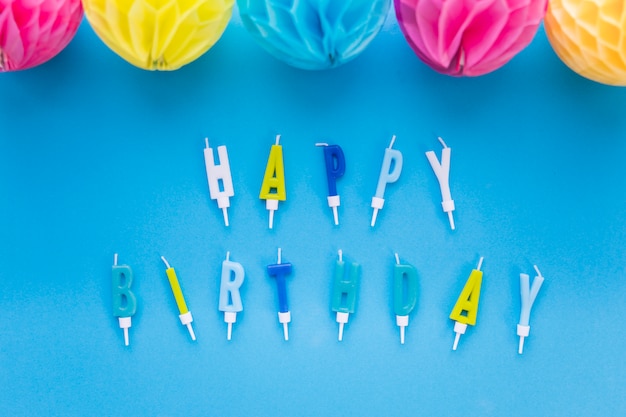 Foto grátis bolas de papel colorido decorativo e feliz aniversário texto velas sobre fundo azul