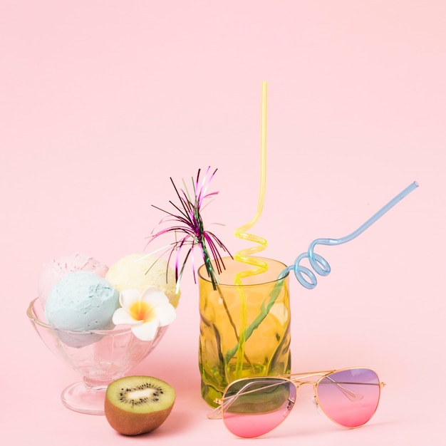 Bolas de sorvete na taça perto de óculos escuros e vidro com varinha ornamental e palhas