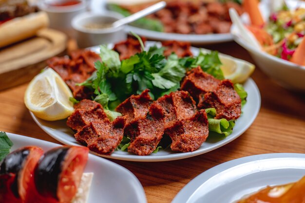 Bolas de tártaro de bife vegetariano de vista lateral com verduras e fatias de limão em um prato