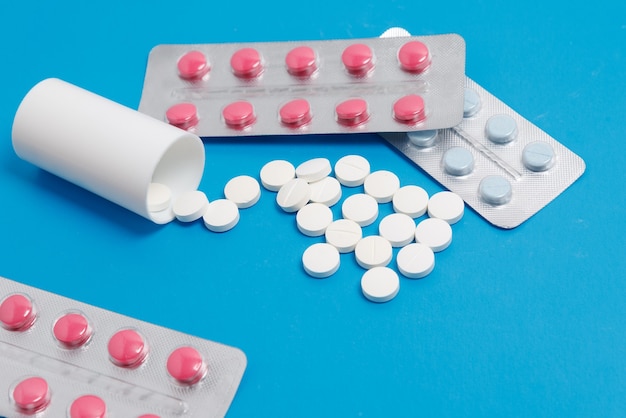 Bolhas com cápsula de rosa e comprimidos redondos brancos sobre fundo azul, conceito de farmácia médica