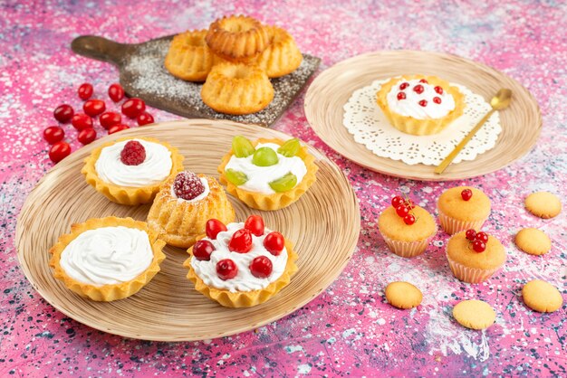 Bolinhos de frente com creme de leite fresco e frutas na superfície brilhante.