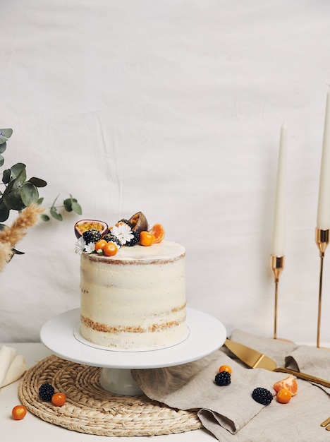 Bolo branco com frutas vermelhas e maracujá ao lado de uma planta atrás de um branco