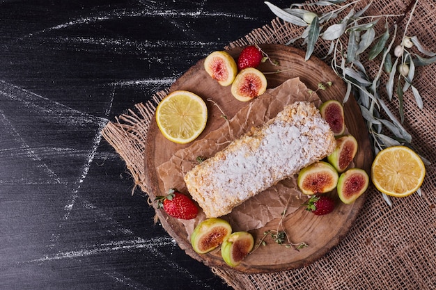 Bolo caseiro rodeado por várias frutas em uma bandeja de madeira redonda.