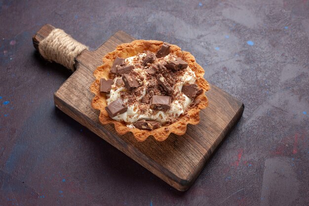 Bolo cremoso de vista frontal com pedaços de chocolate na superfície escura