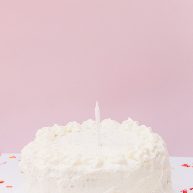 Foto grátis bolo de aniversário branco com uma única vela contra um fundo rosa