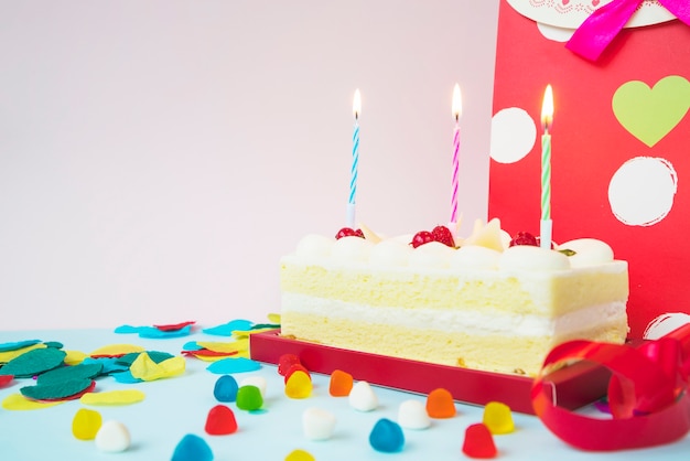 Bolo de aniversário com velas acesas; doces e sacola de compras