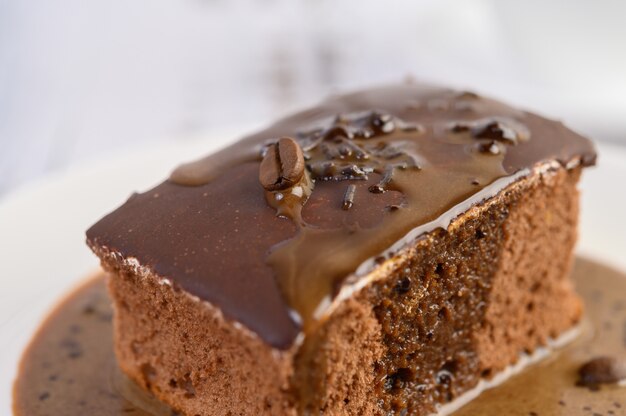 Bolo de chocolate coberto com café em um prato branco com grãos de café em uma mesa de madeira.