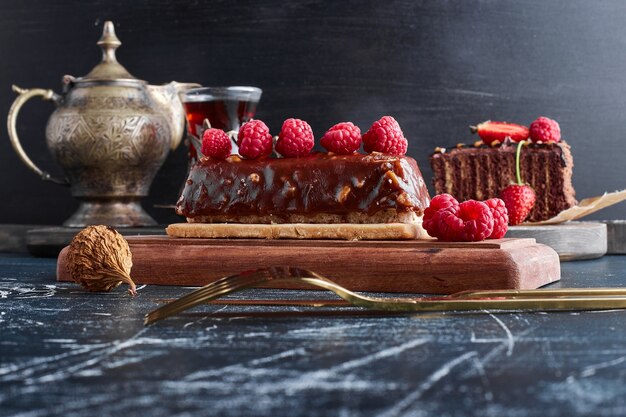 Bolo de chocolate com framboesas em uma placa de madeira.