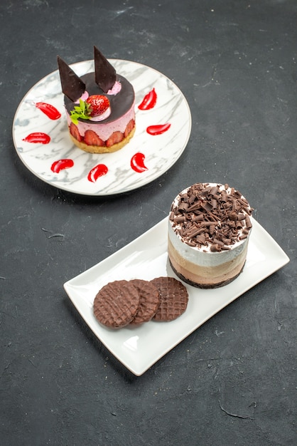 Bolo de chocolate e biscoitos em um prato retangular branco de frente e cheesecake de morango em um prato oval branco